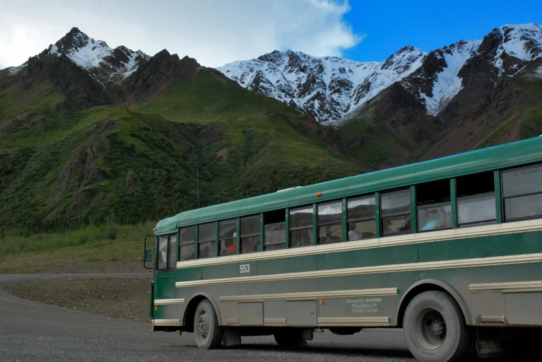 green school bus on a mountainous highway during the day