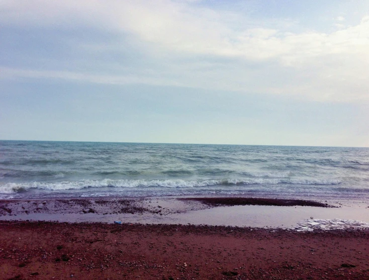 a view of a beach and ocean water with footprints on the ground