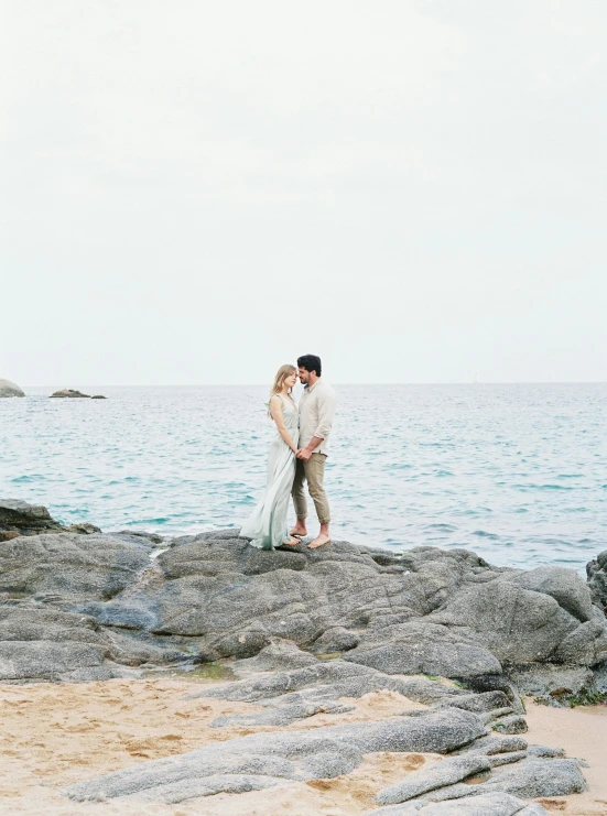 a bride and groom standing on rocks looking out at the ocean