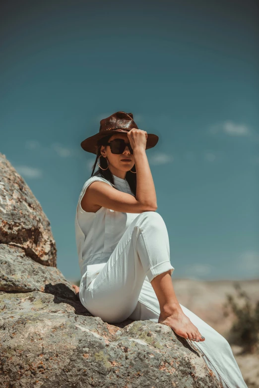 a woman sitting on top of a rock wearing sunglasses