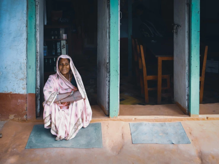 an indian woman sitting in front of a teal blue door