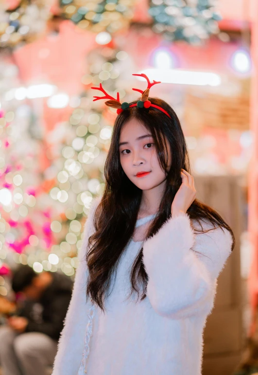 girl posing in front of christmas tree wearing reindeer antlers