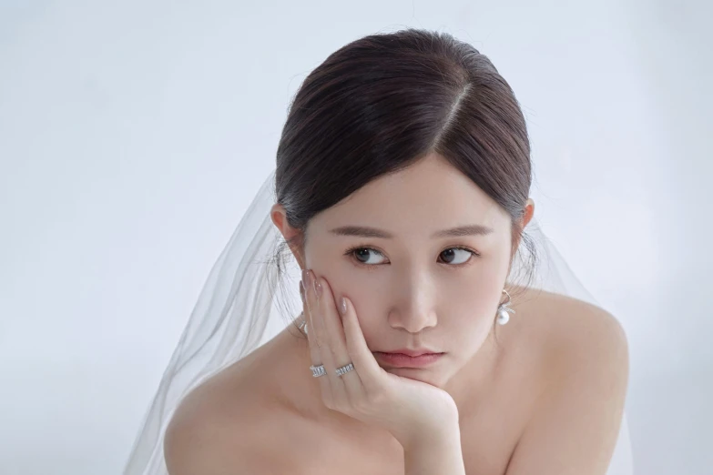 the asian bride with a white veil is touching her cheek