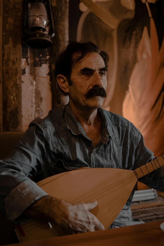 a man sitting in front of a table while holding an acoustic instrument