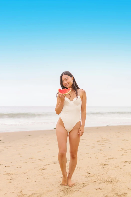 a woman in a white bodysuit on a beach holding a frisbee