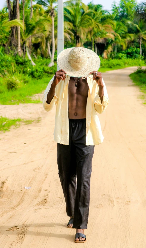 man walking on dirt road with his hat above his head