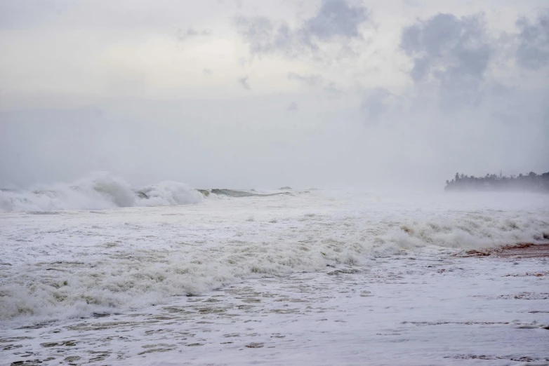 large waves crash onto the beach as two people stand on the shore