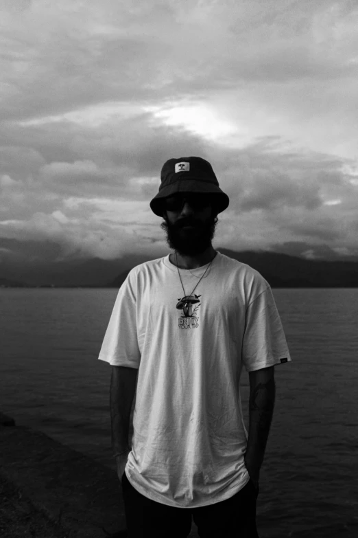 man wearing shirt and hat next to water under a cloudy sky