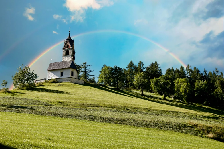 the rainbow over a church sits on a hill