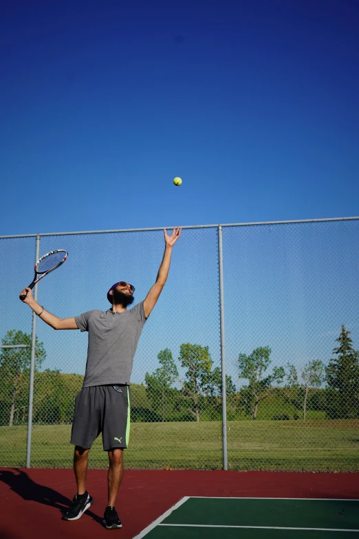 a man wearing a cap stands on one knee as he holds his racket in the air as a ball flies above him