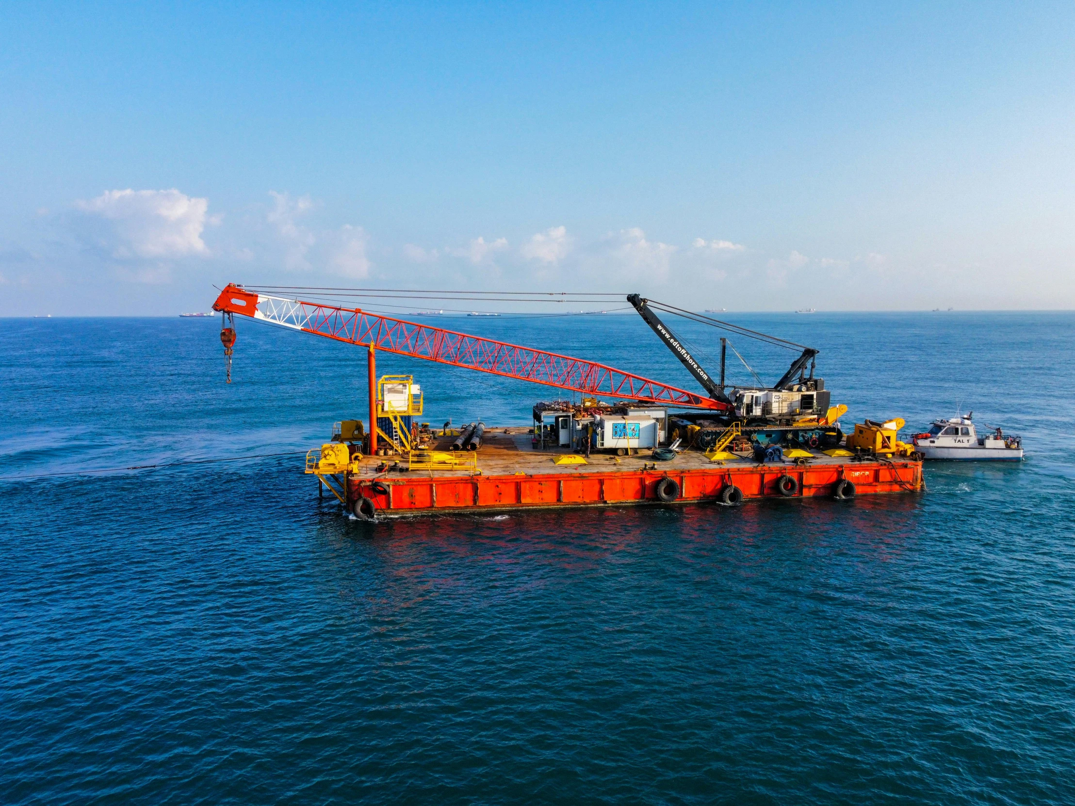 an orange crane on an oil rig with a boat in the water behind it