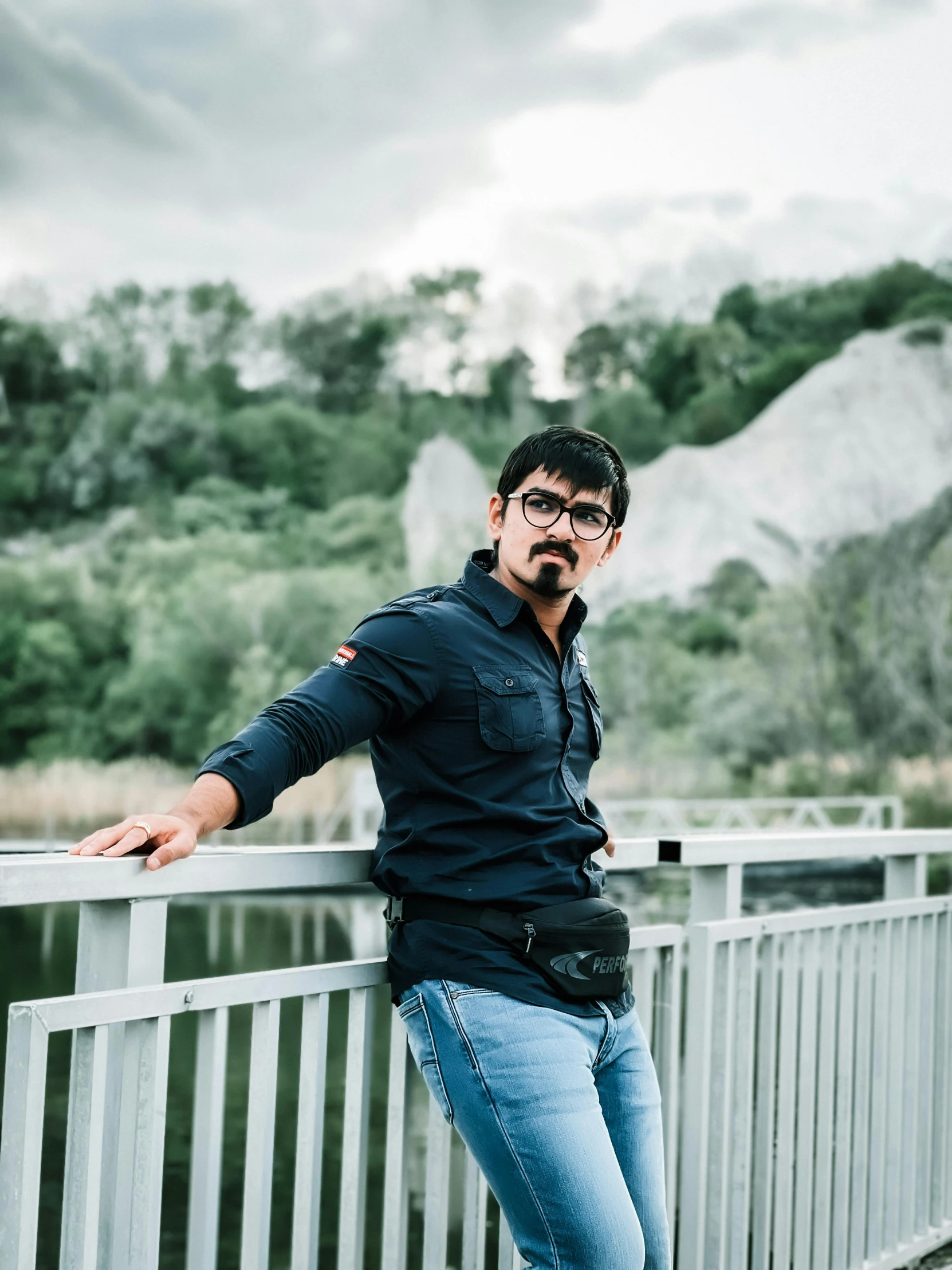 an indian man standing on a bridge with his arms crossed and both wearing glasses