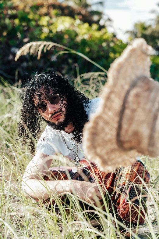 a man with long hair sitting in grass