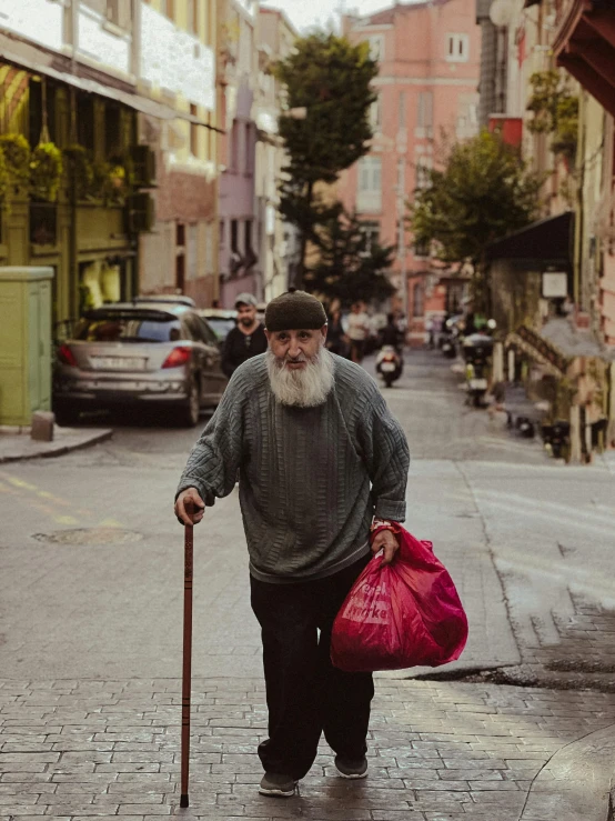 an old man with a cane and bag walks down the street