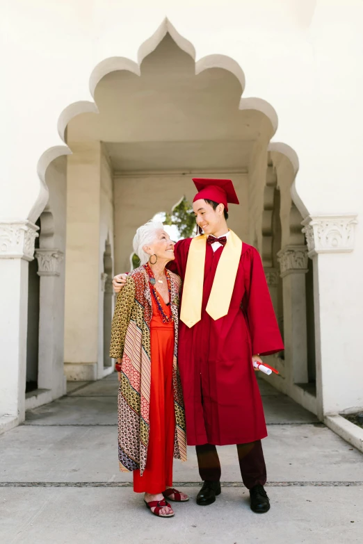 a woman in red dress standing next to a man in a graduation gown