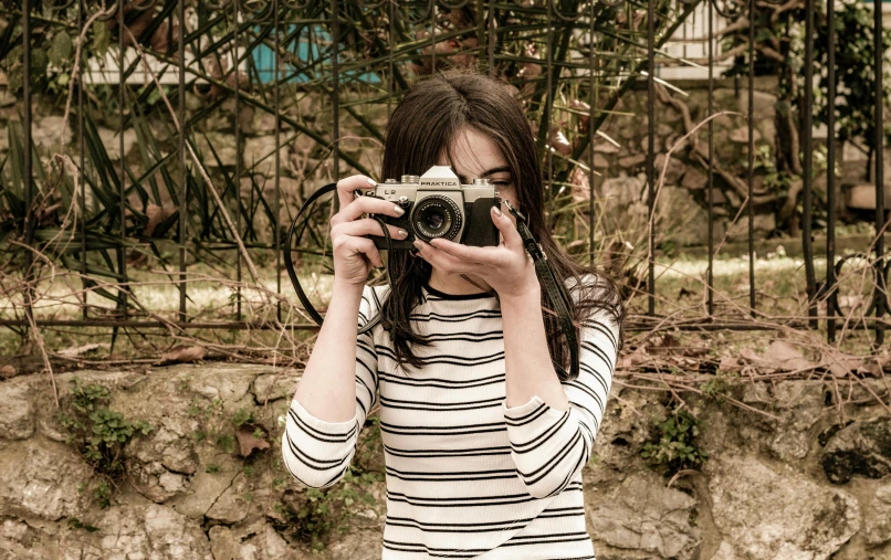 woman taking pograph in front of fence, holding camera up in front of her face