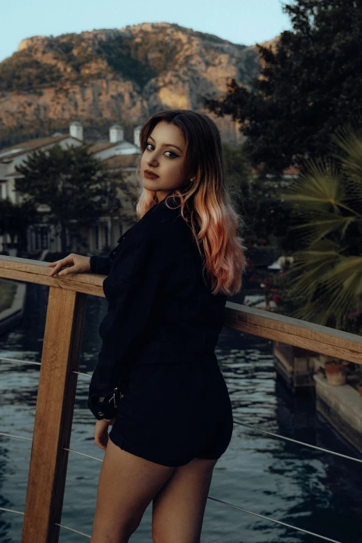 a girl stands against a railing overlooking a body of water