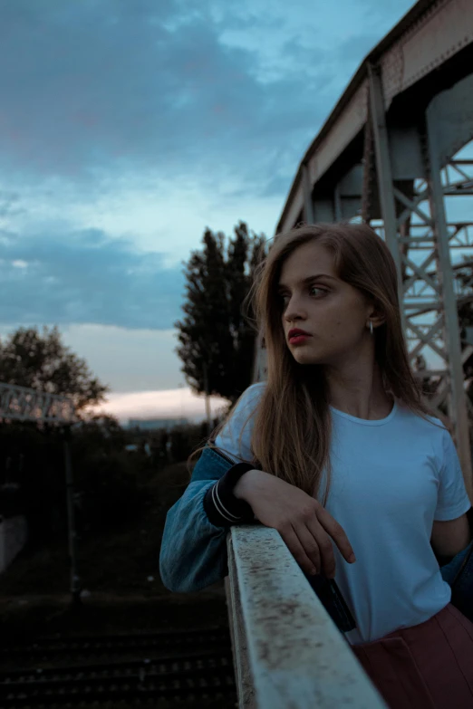 a woman leans against the side of an old train bridge at dusk