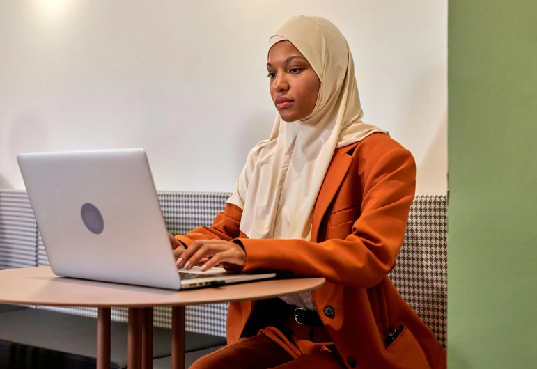 a woman in an orange jacket using her laptop