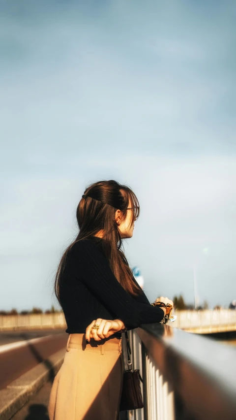 the woman is leaning on the fence with her back turned