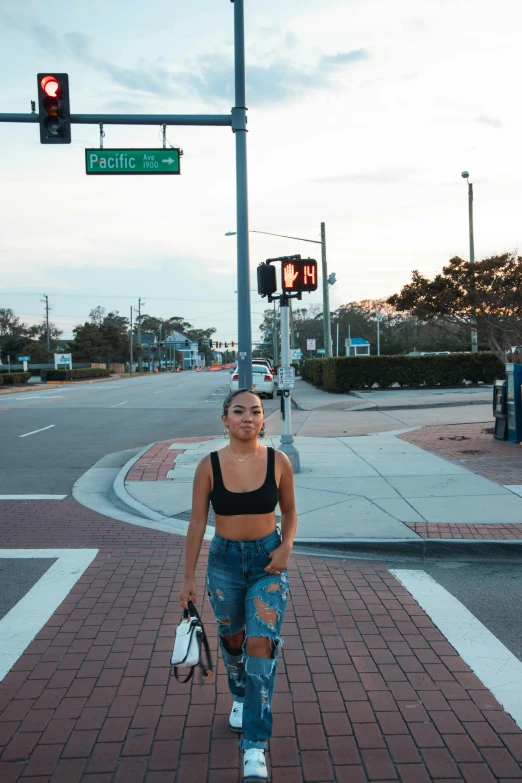 a woman with torn jeans crosses the street near an intersection