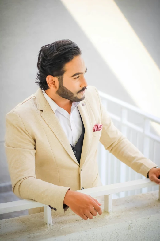 a man wearing a cream colored suit is leaning on a rail