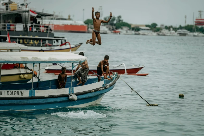 a man jumps from the top of a boat while others are rowing in the water