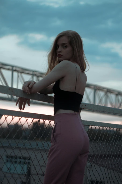 woman leaning on a fence in front of a cloudy sky