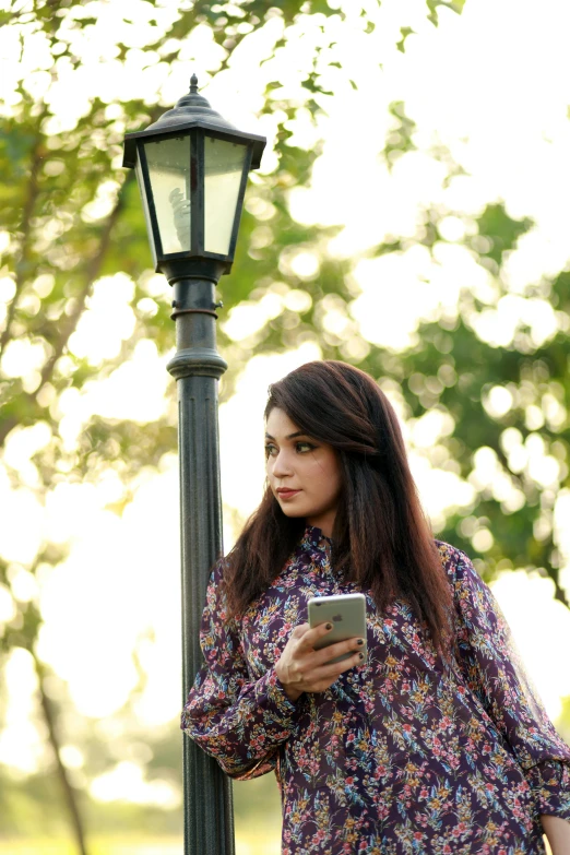 woman leaning on a light post using her cell phone