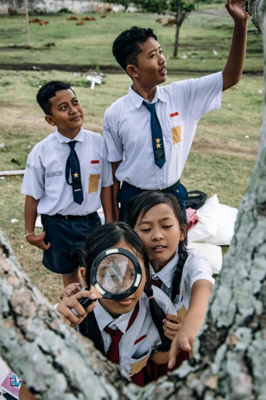 three young s look at the grass through a magnifying glass