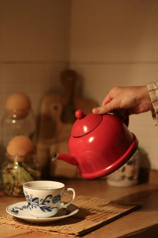 a person's hand pouring out a teapot into a teacup on a tray in a kitchen