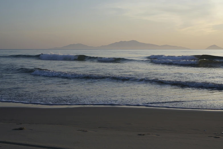 the sun is setting over the ocean with mountains in the distance