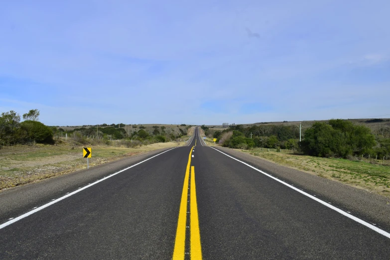 a long road with yellow street markings under a blue sky