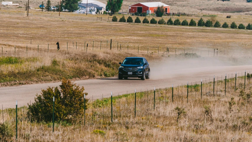 a car drives down the dirt road in a rural countryside