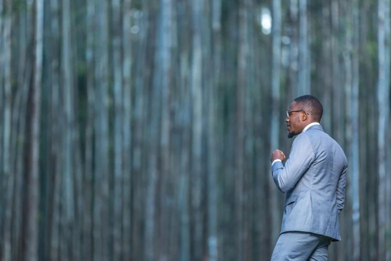an image of man in a suit walking through bamboo forest