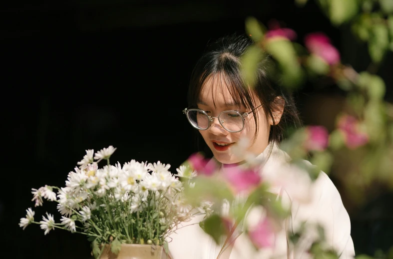 a young woman smiling with glasses holding a vase filled with flowers