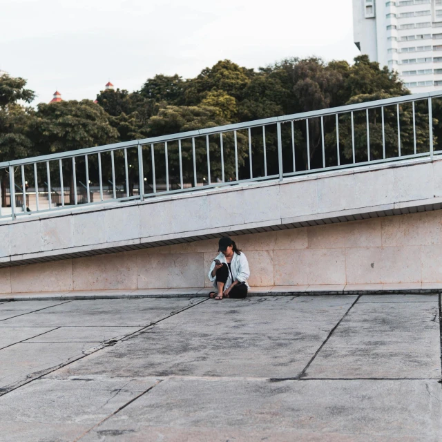 the young man is sitting on the concrete outside with his backpack