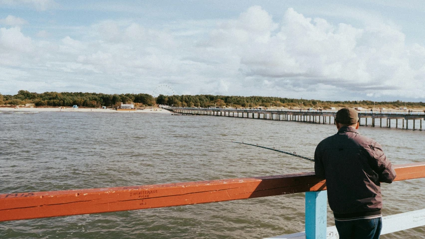 a man standing on a pier fishing with his boat nearby