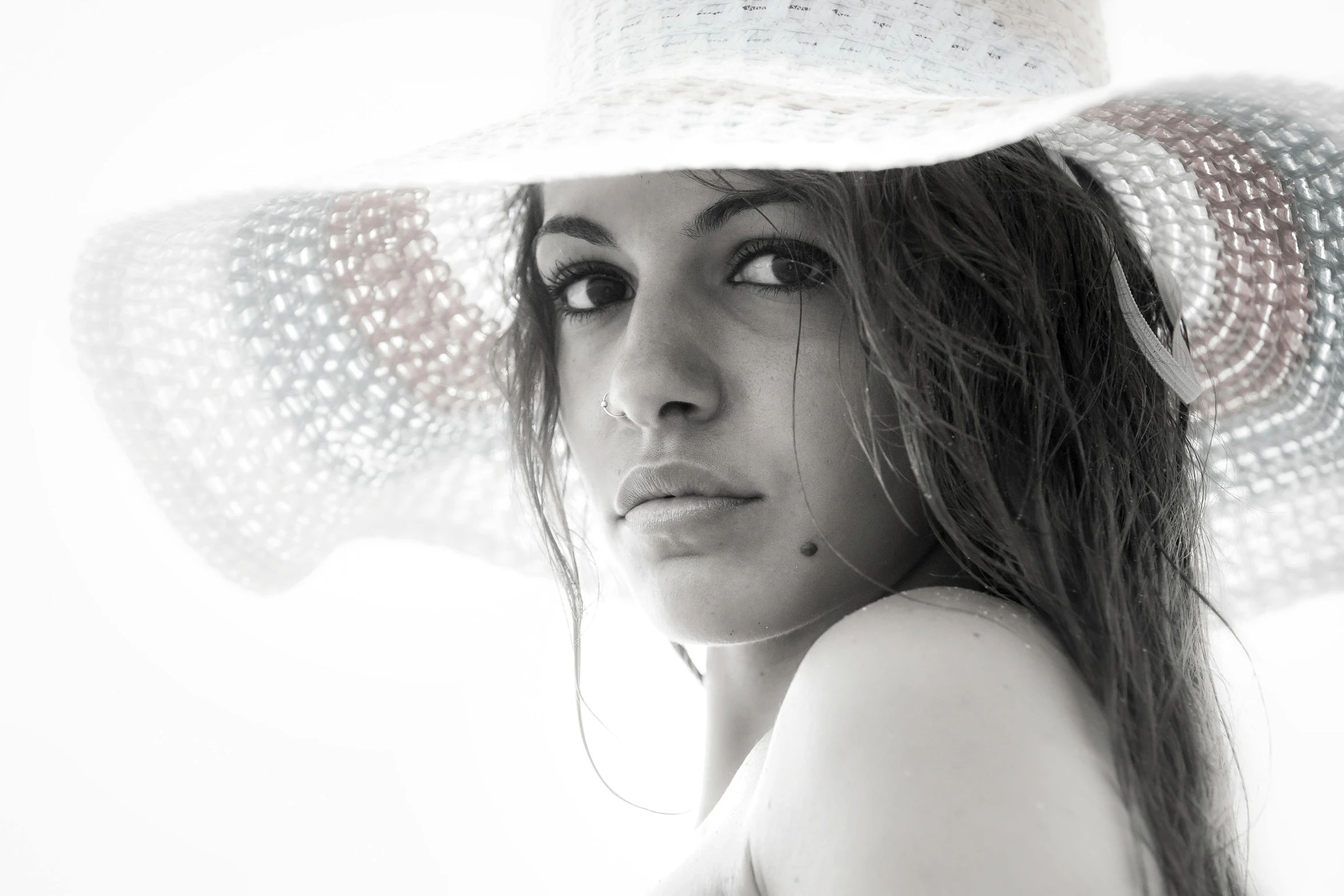 a woman wearing a white hat looking forward with the sun glaring