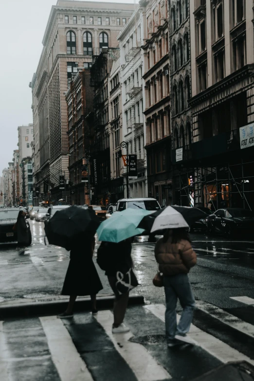 a city street with pedestrians, cars, and buildings and people crossing in the rain