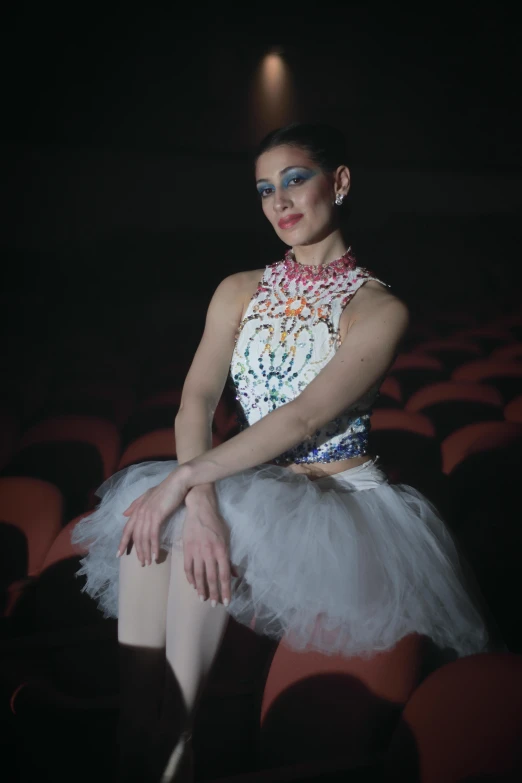 a girl is sitting on a chair with a very long tutu and a costume that features beads