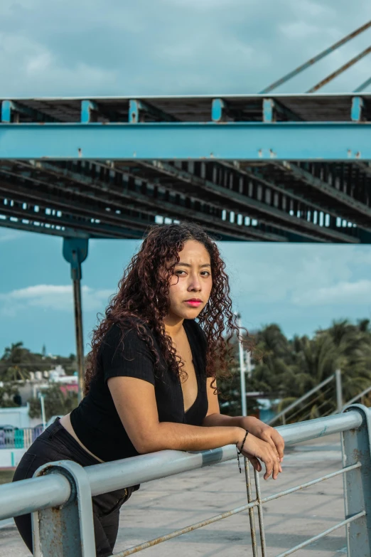 a woman leaning on a metal railing by a bridge