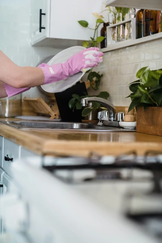 a person cleaning the kitchen sink with a pink glove
