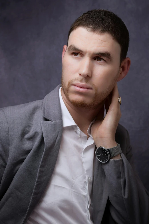 a man in a grey suit leaning against a dark background