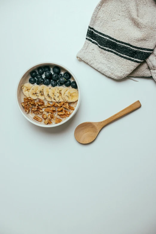 a bowl of blueberries, granola and bananas is on a white table