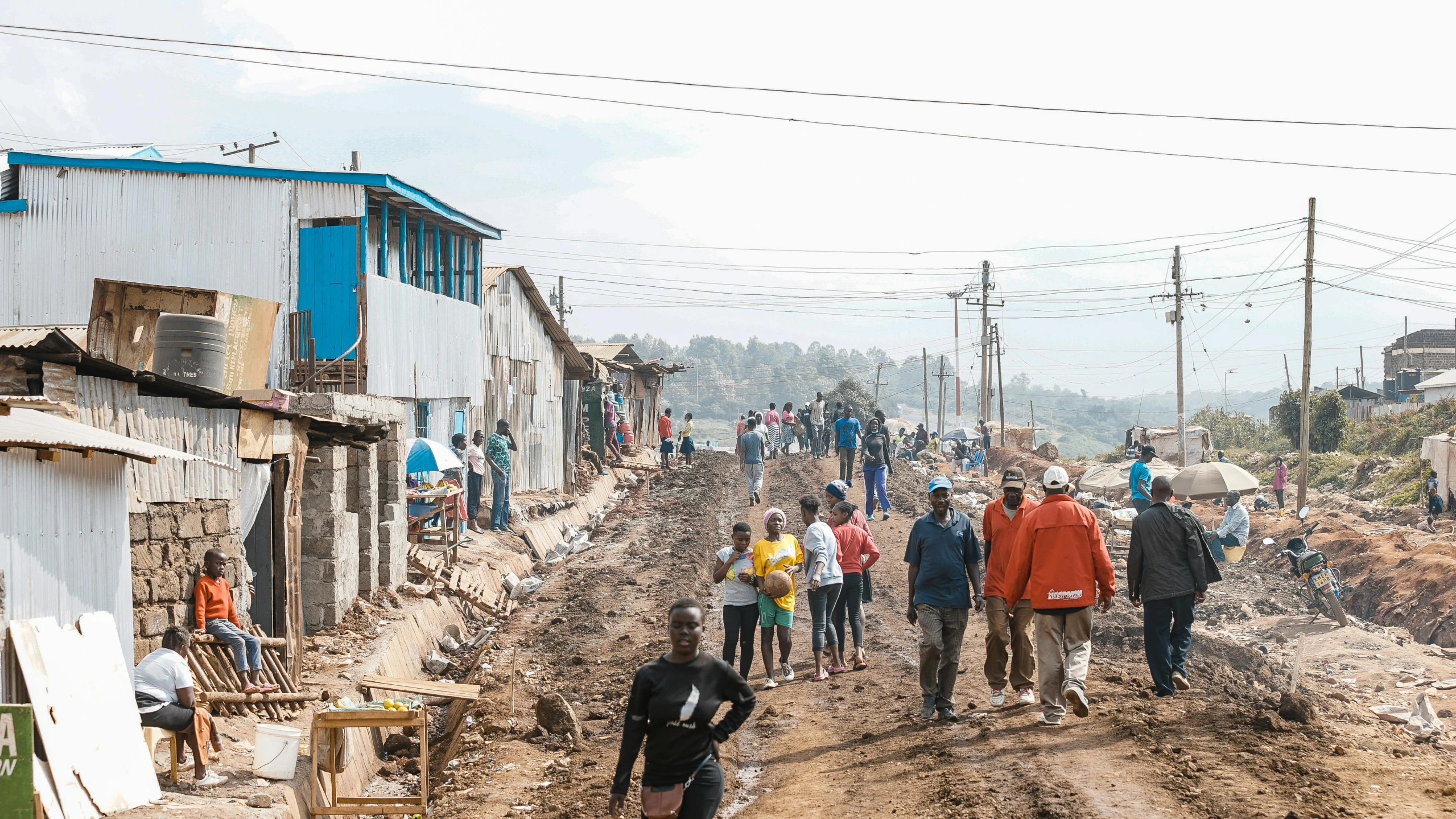 a group of people walking on dirt road next to shacks