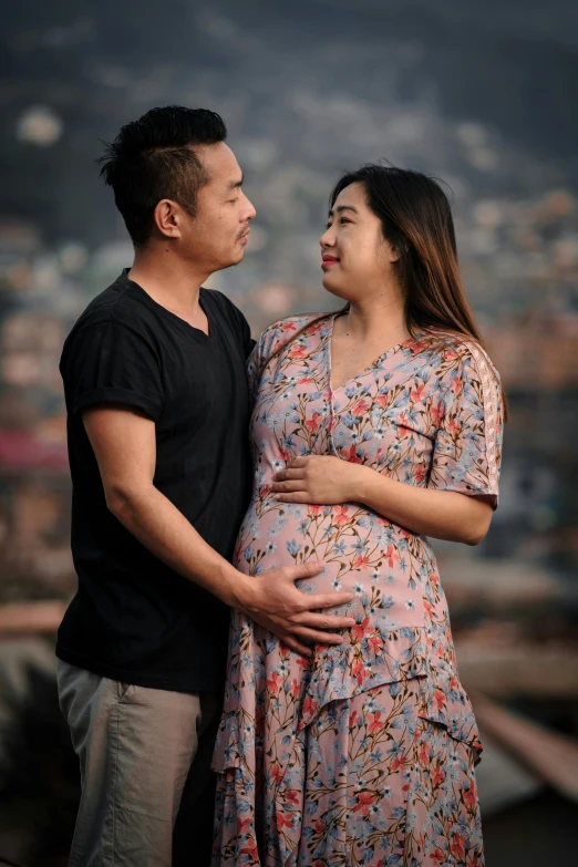 a pregnant asian couple cuddling each other in front of the city backdrop