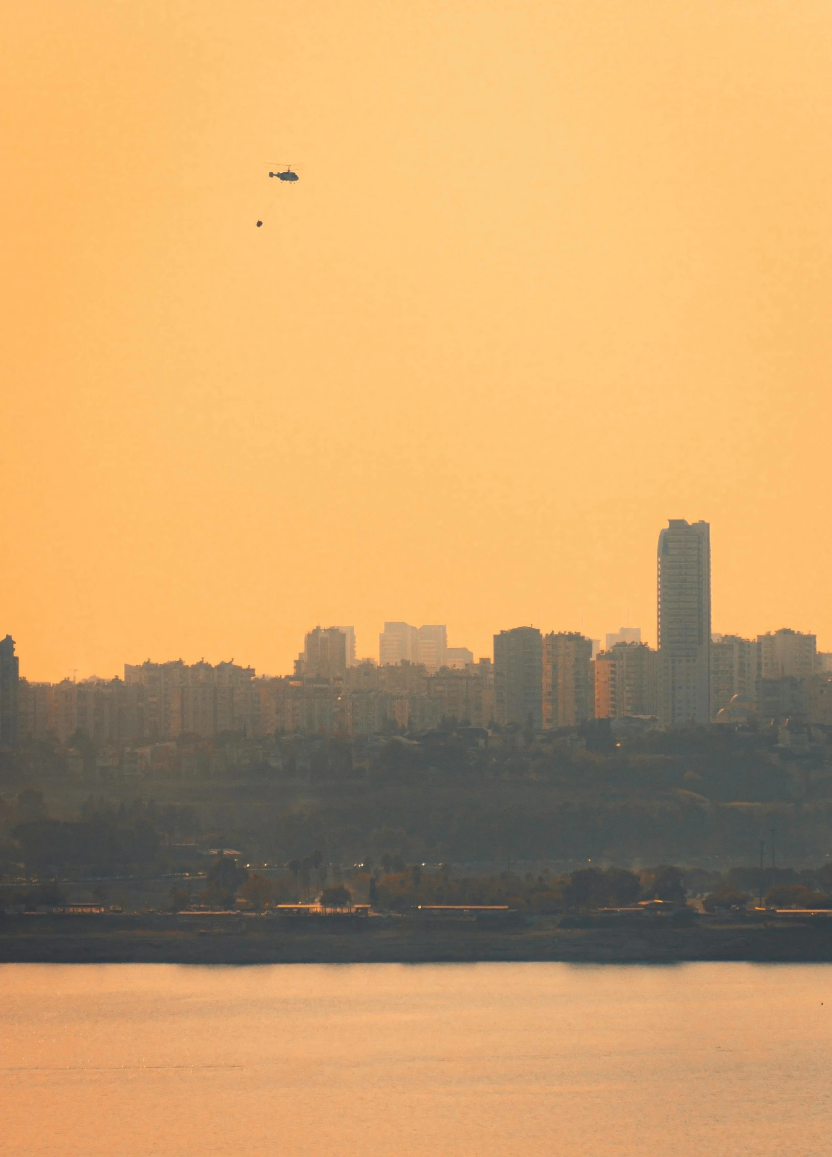 an orange and yellow sky with a plane flying over the city