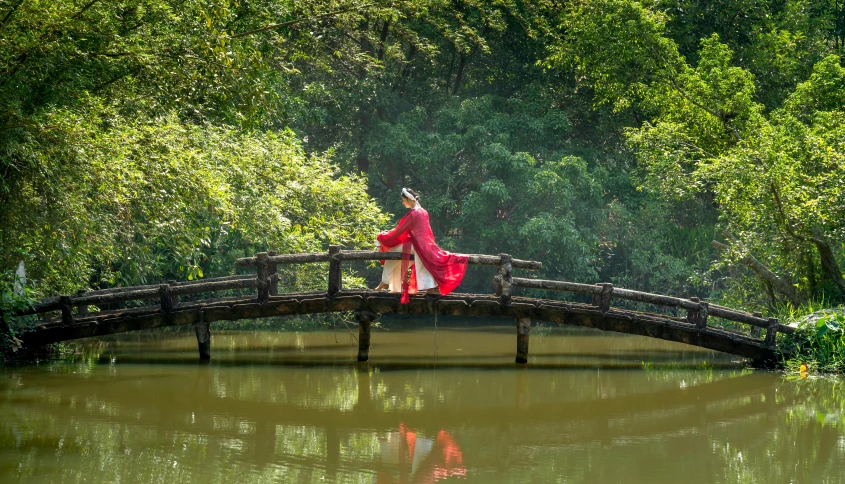 a young woman in a traditional korean dress sits on a bridge over water