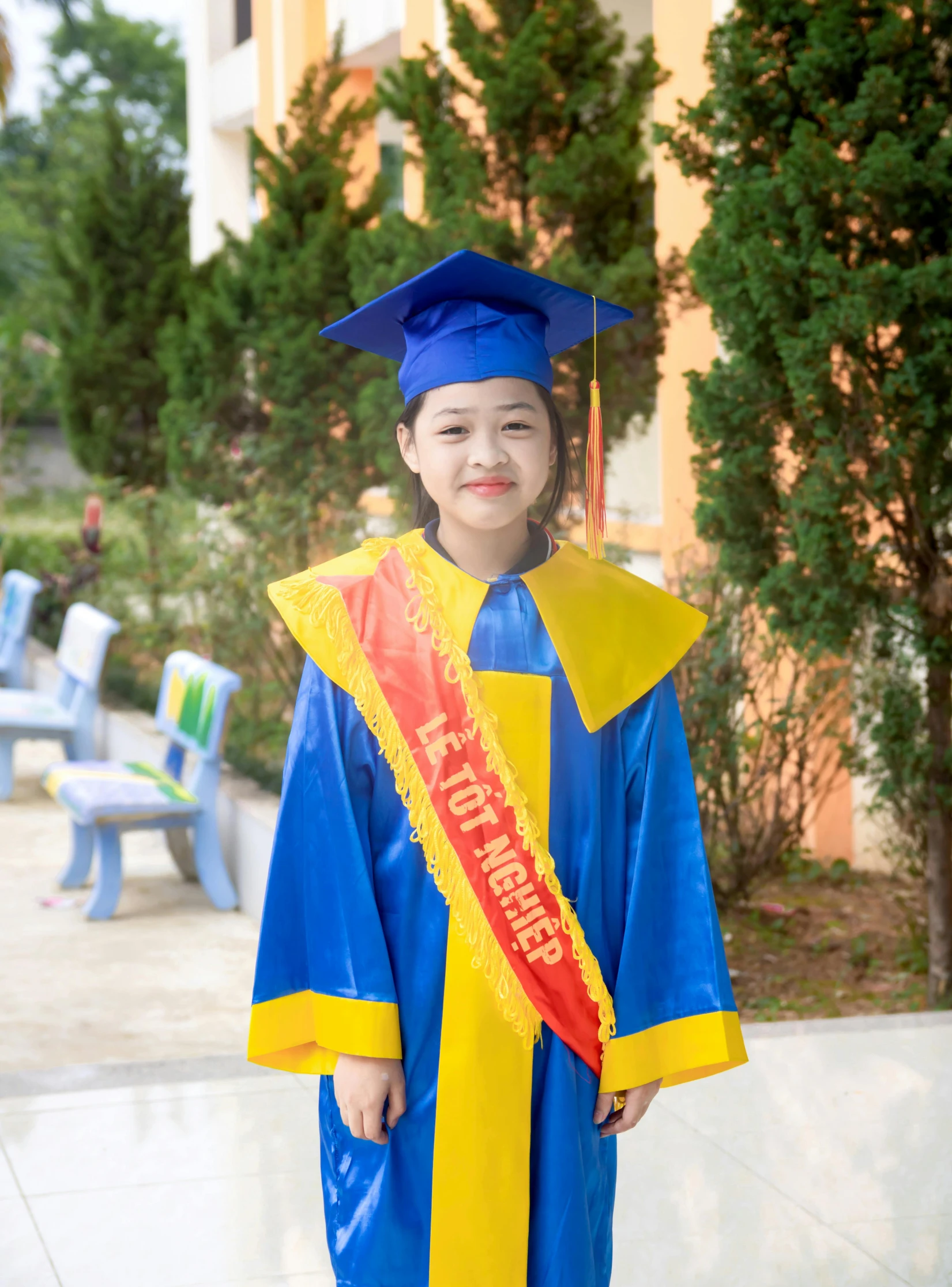 a child in a blue and yellow graduation gown standing in the courtyard